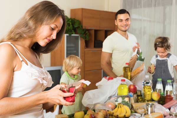 Femme qui regarde son porte monnaie avec sa famille devant les courses alimentaires